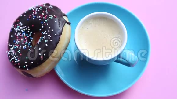 蓝色咖啡杯在旋转的粉红色盘子里放巧克力甜甜圈视频的预览图