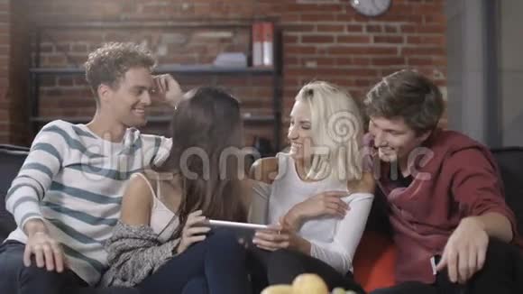 一群快乐的年轻朋友坐在沙发上分享平板电脑视频的预览图
