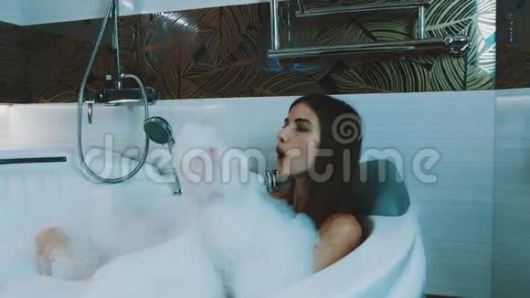 快乐的女孩在浴室里洗了满是泡沫的澡放松点吹肥皂泡沫视频的预览图