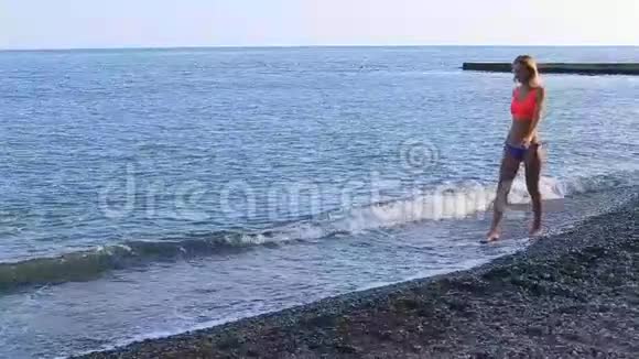 孤独的女孩沿着海滩散步看着地平线视频的预览图
