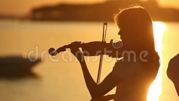 小提琴二重奏在湖上日落时分男人和女人在大自然中拉小提琴视频的预览图