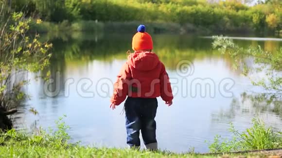 一个孩子站在池塘边扔石头在新鲜空气中游走视频的预览图