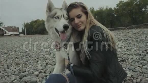 一可爱的女人带着西伯利亚哈士奇狗坐在海岸上视频的预览图