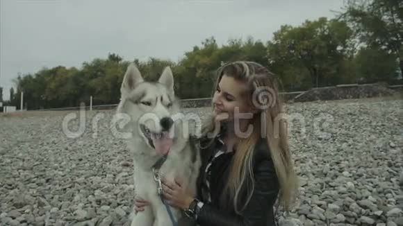 带着西伯利亚哈士奇狗坐在海边的年轻可爱的女人视频的预览图
