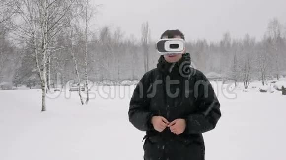 一个人戴着虚拟现实耳机在冬天的雪林大雪纷飞他试图触摸虚拟物体视频的预览图