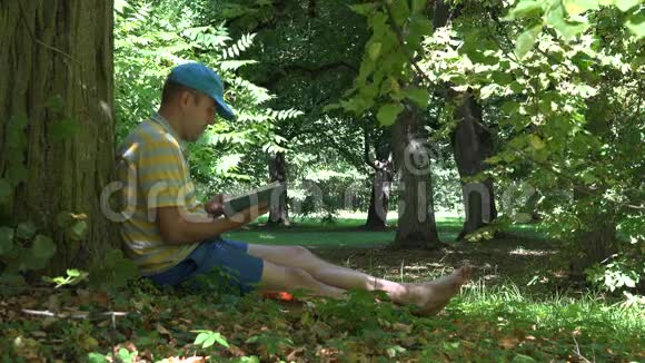 人在公园的老树下度过了他的假期读小说4K视频的预览图