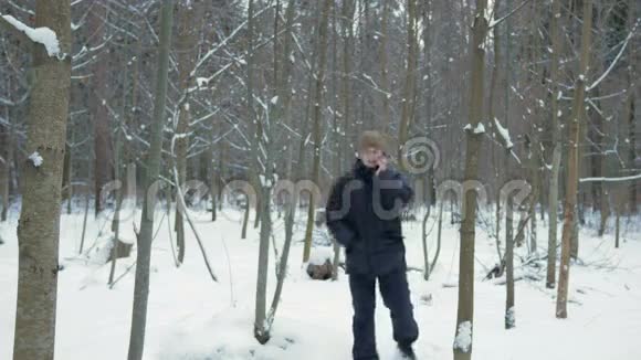 一个年轻人在冬天的森林里打电话他停下来结束了谈话穿深色夹克的男人视频的预览图