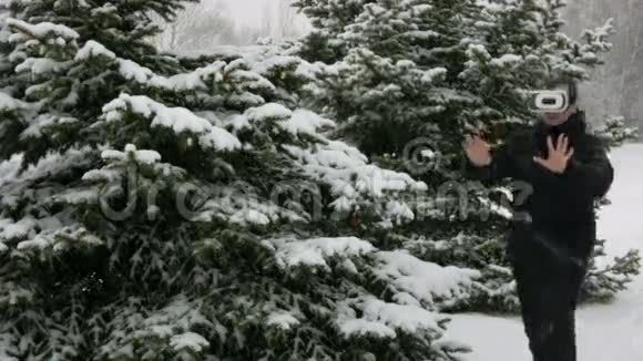 一个人戴着虚拟现实耳机在冬天的雪林大雪纷飞他试图触摸虚拟物体视频的预览图
