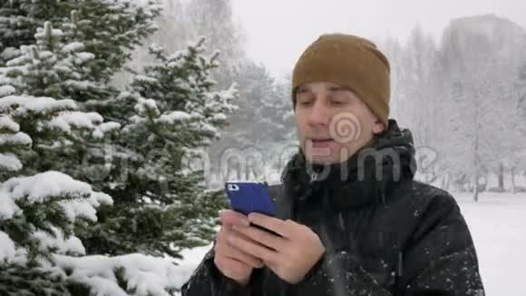 在冬天的雪林里年轻人在电话里打短信大雪纷飞他微笑着说出文字视频的预览图
