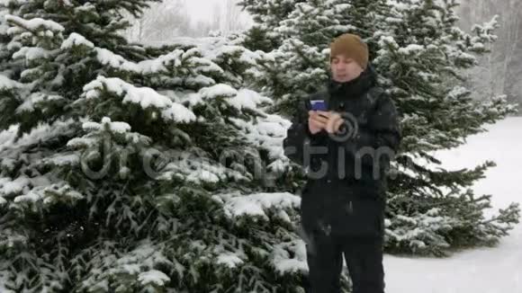 在冬天的雪林里年轻人在电话里打短信大雪纷飞他微笑着说出文字视频的预览图