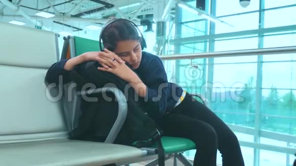 戴着耳机的少女睡在机场等待飞机起飞登机口的长椅上视频的预览图