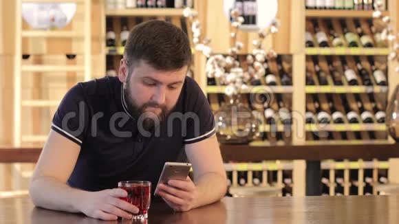 男人在餐馆或咖啡馆喝红色饮料年轻人在喝红色鸡尾酒时用智能手机视频的预览图