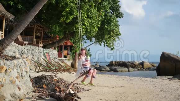 一个女孩和一个孩子在海滩上的绳子秋千上摇摆视频的预览图