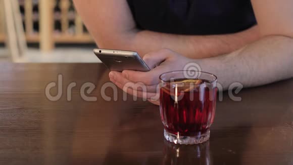 男人在餐馆或咖啡馆喝红色饮料年轻人在喝红色鸡尾酒时用智能手机视频的预览图