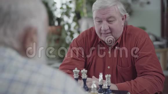 两个成熟的男人坐在家里下棋高加索老人和朋友在室内愉快地下棋视频的预览图