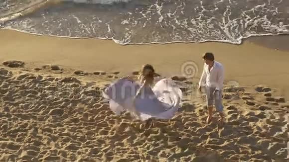 年轻浪漫的一对美丽的女孩穿着淡粉色长裙在沙滩上为她的男朋友跳舞激情时刻视频的预览图
