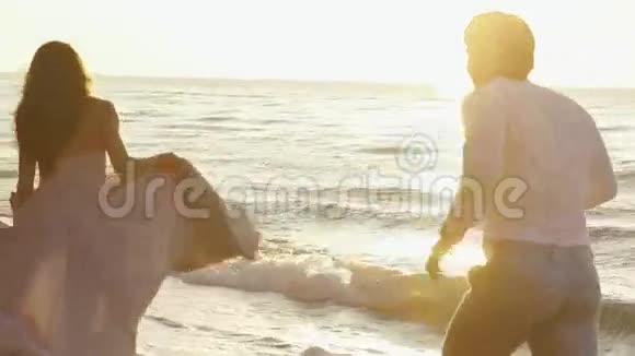 年轻浪漫的一对漂亮的女孩穿着淡粉色的长裙英俊的男人在沙滩上沿着海岸嬉戏视频的预览图