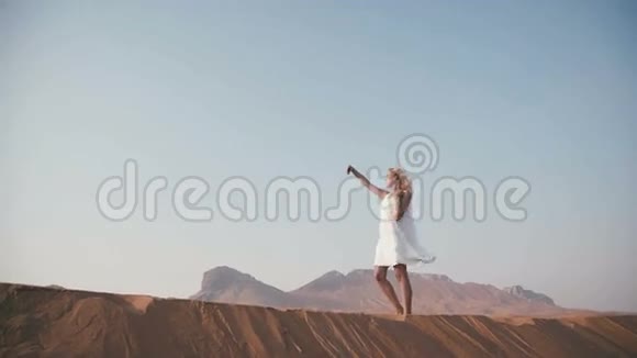穿着白色连衣裙的年轻女子在沙漠中散步欣赏风景视频的预览图