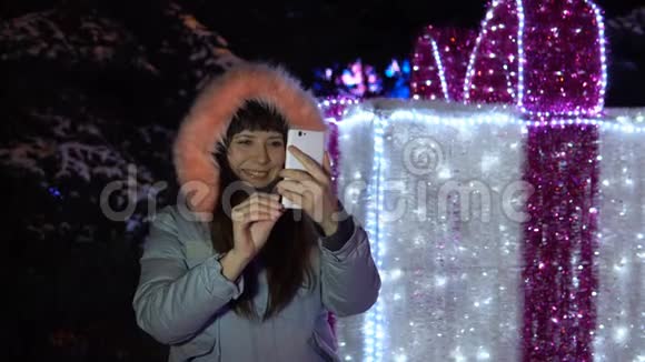 年轻女子正在使用手机而站在一个巨大的闪闪发光的礼物旁边视频的预览图