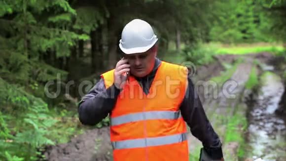 森林官员在车辙的森林道路上用手机交谈视频的预览图