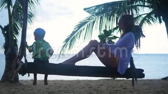 一个女孩和一个孩子在海滩上的绳子秋千上摇摆视频的预览图