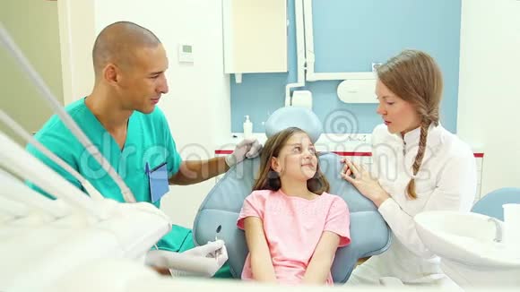 可爱的小女孩与牙医和助手交谈展示她的疼痛牙齿视频的预览图