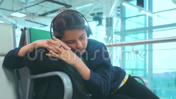 一个戴着耳机的少女睡在机场等着飞机起飞的大门长椅上的旅行者视频的预览图