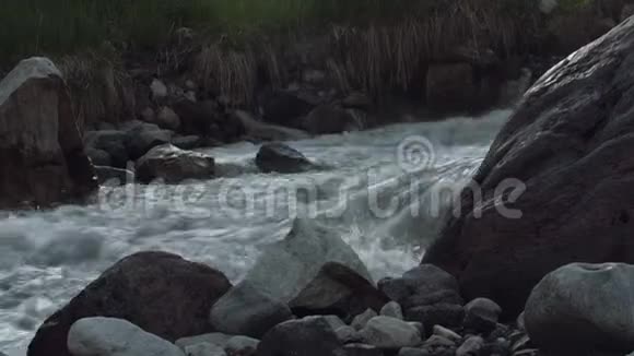 湍急的小溪在高高的岩石山上积雪覆盖着绿色的灌木丛视频的预览图