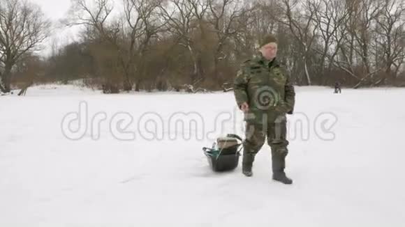 一位老人在冬天进入一个冰冻的湖把东西放在雪橇上穿着土黄色暖衣的男人视频的预览图
