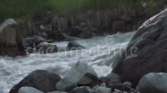 湍急的河流在高高的岩石山上覆盖着白雪绿灌木丛视频的预览图
