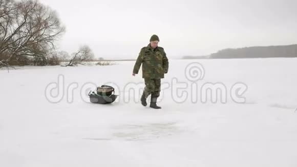 一位老人在冬天进入一个冰冻的湖把东西放在雪橇上穿着土黄色暖衣的男人视频的预览图