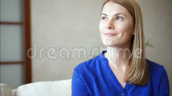 一幅美丽迷人的年轻女子穿着蓝色衬衫坐在客厅沙发上微笑的画像视频的预览图