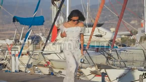 美丽的年轻女子穿着白色长裙在船旁边的港口奔跑视频的预览图