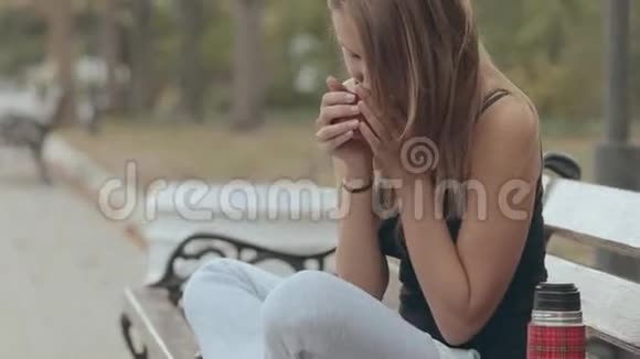 坐在公园长椅上喝热茶的女孩视频的预览图