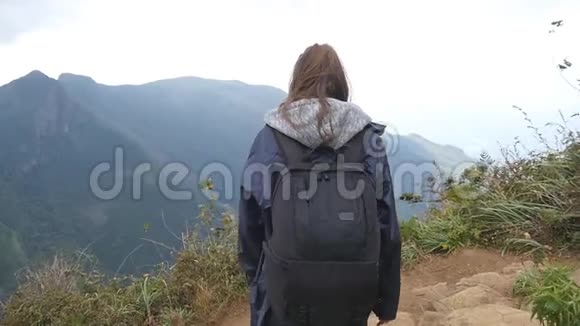 年轻的女徒步旅行者背包伸向山顶举起双手穿着雨衣的女游客站在视频的预览图