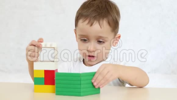 一个孩子正在建造一座彩色积木的房子坐在白色背景的桌子旁孩子和玩具视频的预览图