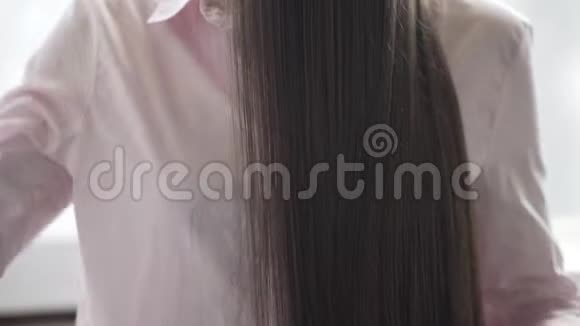 穿着粉红色衬衫的布鲁内特女孩正在梳理她美丽的长发梳子视频的预览图