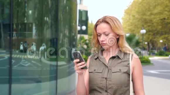 带电话的女孩在一个炎热的晴天在一个现代城市散步摩天大楼的背景4k慢动作视频的预览图