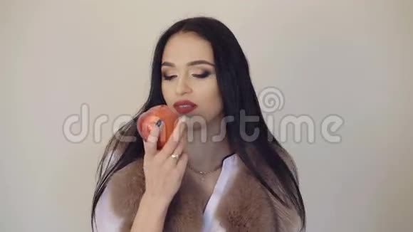 聪明的女孩吃着一个大的深红色的苹果在4K背景上微笑和调情视频的预览图