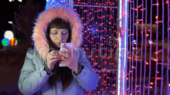 年轻女子正在使用手机而站在一个巨大的闪闪发光的礼物旁边视频的预览图