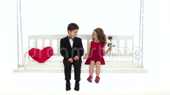 小男孩和小女孩正坐在秋千上可爱地聊天白色背景慢动作视频的预览图