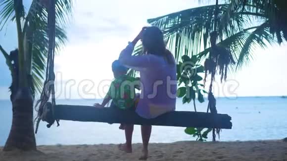 一个女孩和一个孩子在海滩上的绳子秋千上摇摆热带岛屿视频的预览图