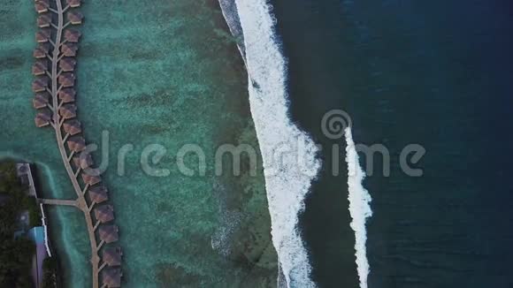 带平房和绿松石印度洋海浪的热带岛屿度假酒店的空中景观视频的预览图