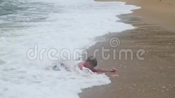 孩子躺在沙滩上沐浴在大海的波涛中视频的预览图