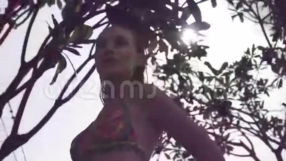 年轻的女人穿着比基尼湿头发在屋顶上阳光明媚的一天蓝天和阳光透过绿色的树木视频的预览图