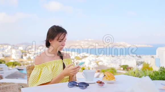 白种人女孩早餐与智能手机在户外咖啡馆令人惊叹的景观Mykonos镇视频的预览图