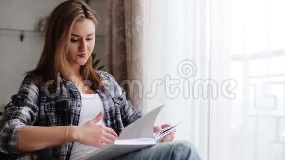 年轻迷人的女士坐在沙发上在家里看书视频的预览图