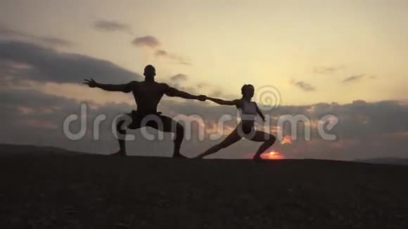 在山顶日落时做体操运动的运动型肌肉男教练的剪影视频的预览图