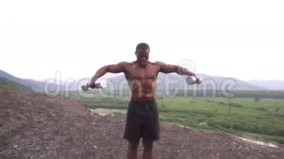 黑人非裔美国人肌肉男赤裸的躯干在多云的天空背景下举起哑铃视频的预览图