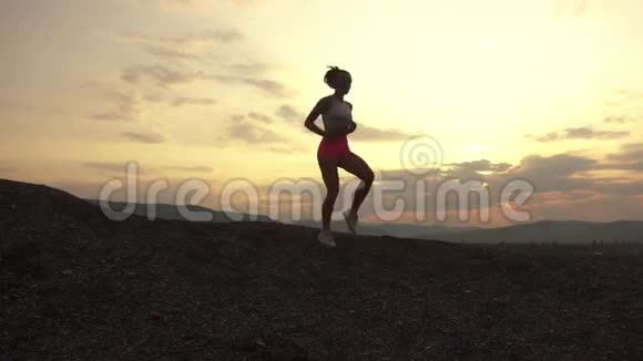 适合女性跑步者的剪影完美的肌肉身体在日落时在户外慢跑山地景观背景视频的预览图